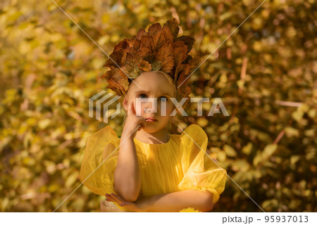 A little girl in a fluffy yellow dress. Little princess with blue eyes among the leaves and bushes 95937013