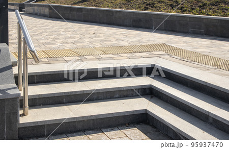 Close-up of granite stone steps located at an angle, in a metal railing, outdoors, in a city park Close-up of granite stone steps located at an angle, in a metal railing, outdoors, in a city park 95937470