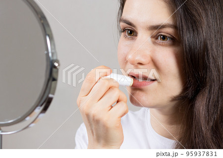 A beautiful woman in front of a mirror paints her lips with a natural lip balm. Cosmetics without plastic from environmentally friendly means A beautiful woman in front of a mirror paints her lips with a natural lip balm. Cosmetics without plastic from environmentally friendly means 95937831