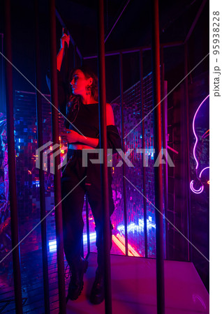 Caucasian woman in neon studio behind steel bars.  95938228