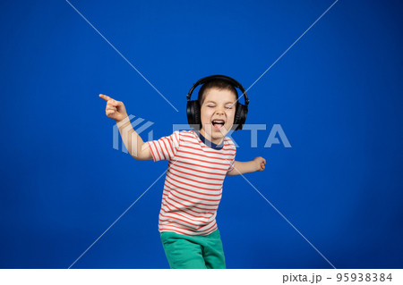 Happy smart 5 year old boy in big black headphones points fingers to the sides in place for text copy space 95938384