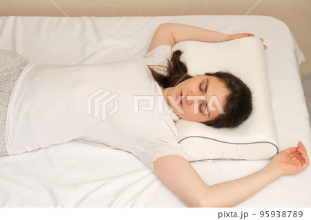 A woman sleeps on an orthopedic pillow made of memory foam, lying on a bed. The correct pillow for a comfortable healthy sleep. 95938789