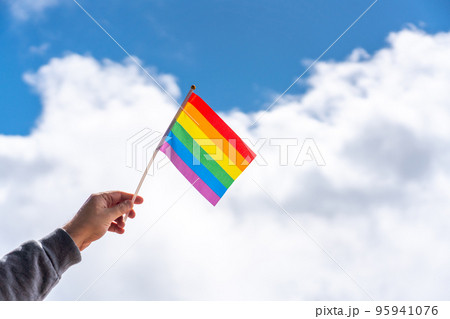 Inclined hand holds in fingers in the wind LGBT flag on a cloudy background Inclined hand holds in fingers in the wind LGBT flag on a cloudy background 95941076