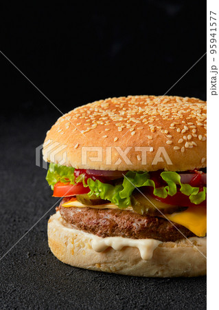 Close up classic traditional cheeseburger with beef, tomato, lettuce, pickles and onion on black background 95941577