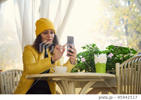 Stylish woman using mobile phone while a coffee break in a cafe. Reading news, social network, surfing the internet, scrolling newsfeed, checking content in social media in smartphone. Coffee break Stylish woman using mobile phone while a coffee break in a cafe. Reading news, social network, surfing the internet, scrolling newsfeed, checking content in social media in smartphone. Coffee break 95942517