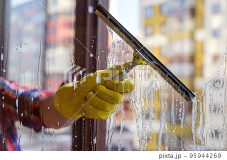 Scraper for washing windows in hands in yellow gloves. Wash the dirty and dusty windows in the spring 95944269