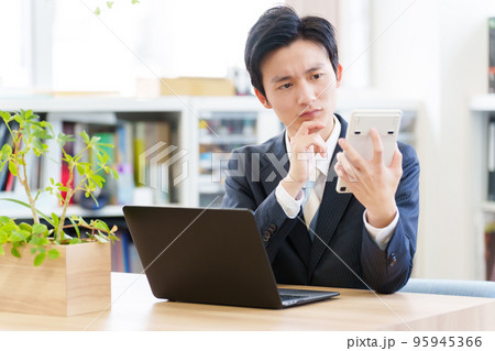 電卓を見ながら悩むビジネスマン 95945366