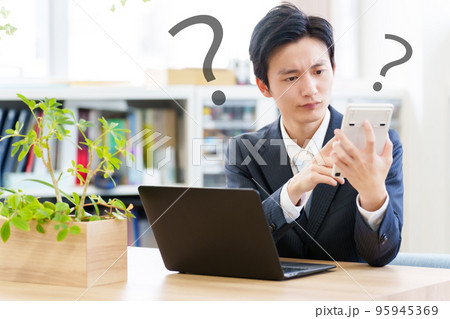 電卓を見ながら悩むビジネスマン 電卓を見ながら悩むビジネスマン 95945369