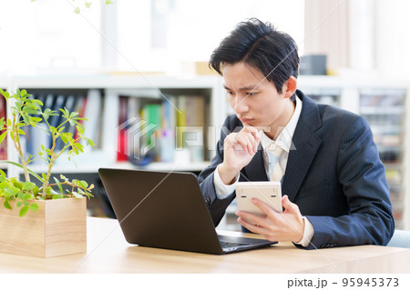 電卓を見ながら悩むビジネスマン 95945373