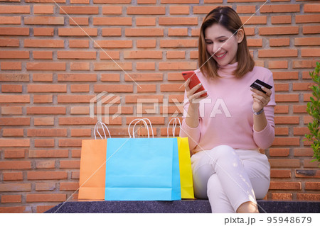 Young woman buys online with smartphone and credit card with colorful shopping bags next to it. 95948679