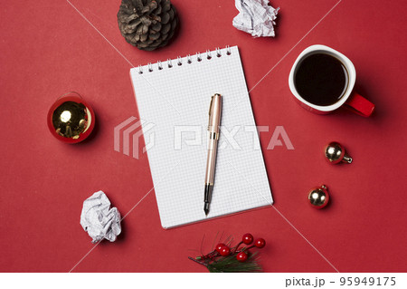 a notepad, pen and christmas decorations on a red surface with coffee mugs and pine cones in the background 95949175