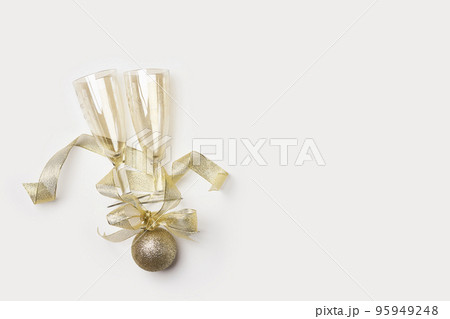 two champagne flutes on a white surface with gold ribbons around them and the wine bottle is in the foreground 95949248