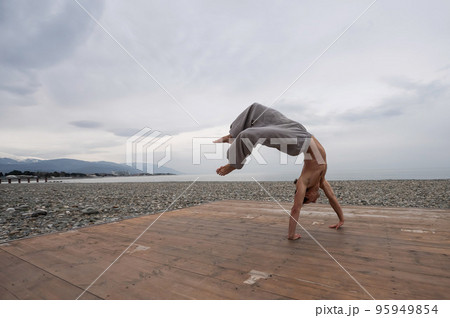 Shirtless caucasian man doing backflip on pebble beach. Shirtless caucasian man doing backflip on pebble beach. 95949854