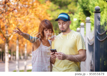 Young couple using a smartphone app with online map. Caucasian woman with tattoos shows a direction. The concept of relationship psychology and city travel 95955679