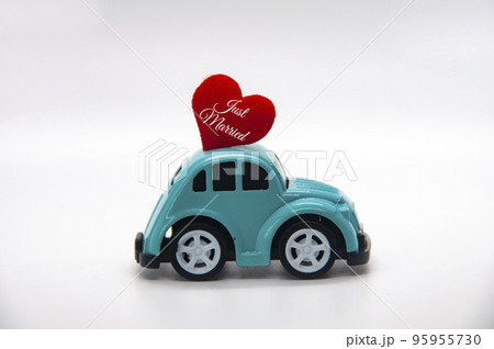 Mini toy car carrying red heart shape with text Just Married. Newly wed couple concept. Mini toy car carrying red heart shape with text Just Married. Newly wed couple concept. 95955730
