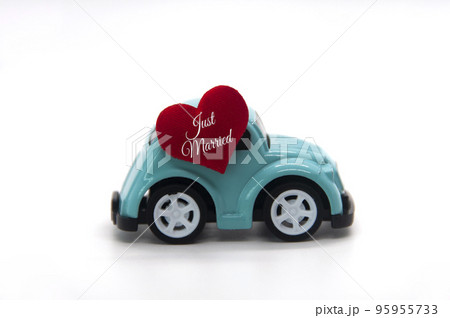 Mini toy car carrying red heart shape with text Just Married. Newly wed couple concept. Mini toy car carrying red heart shape with text Just Married. Newly wed couple concept. 95955733