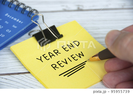 Year end review text on yellow notepad with December calendar background. Year end closing and review concept. Year end review text on yellow notepad with December calendar background. Year end closing and review concept. 95955739