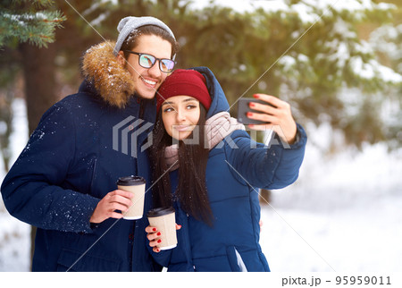 winter holidays, hot drinks and people concept. happy young couple with coffee in winter forest. winter holidays, hot drinks and people concept. happy young couple with coffee in winter forest. 95959011