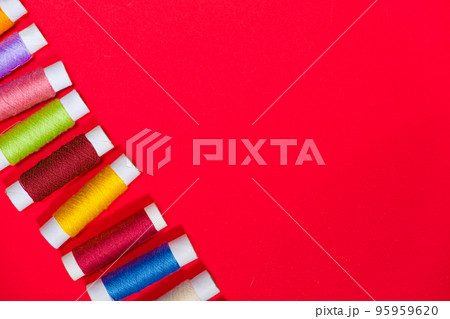 A set of multi-colored threads for sewing with an empty space for text on a red background, top view. Tailoring and needlework equipment, tailor banner. A set of multi-colored threads for sewing with an empty space for text on a red background, top view. Tailoring and needlework equipment, tailor banner. 95959620
