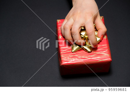 A woman's hand grabs a gift box by a bow on a black background with a place for text. A woman's hand grabs a gift box by a bow on a black background with a place for text. 95959681