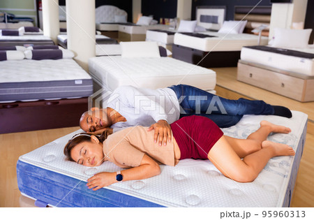 Young latin american couple sleeping on display sample bed with orthopedic mattress in furniture shop Young latin american couple sleeping on display sample bed with orthopedic mattress in furniture shop 95960313