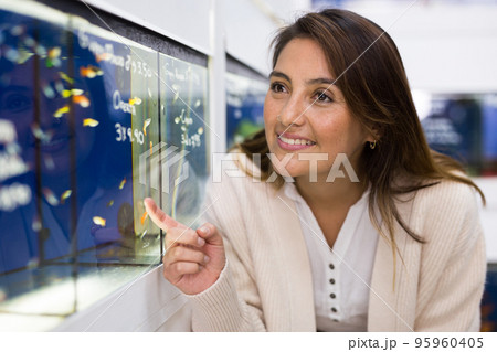 Portrait of interested young woman looking at colorful tropical fish in aquariums in shop 95960405