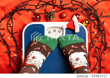 A woman in Christmas socks stands on the scales, weighs herself after gluttony during the holidays 95961417