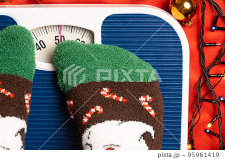 A woman in Christmas socks stands on the scales, weighs herself after gluttony during the holidays 95961419