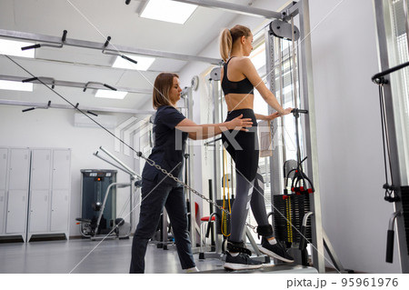 Rehabilitation specialist helping woman to do exercises on decompression simulators at gym Rehabilitation specialist helping woman to do exercises on decompression simulators at gym 95961976