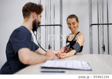 Happy fitness woman on physical examination at sports doctor. .Physiotherapist measures the blood pressure of the girl 95962194