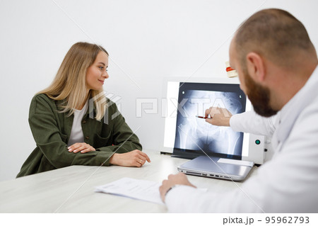 Doctor orthopedist showing x-ray picture to his female patient during consultation in clinic 95962793