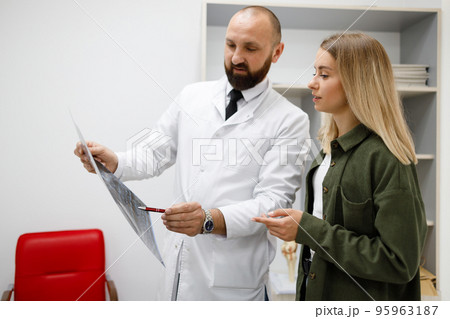 Male doctor explaining xray report to young female patient 95963187