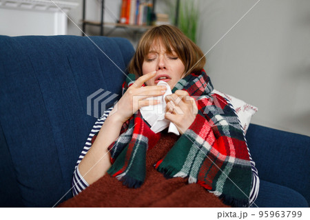 Sick woman with a runny nose lying on a sofa under a blanket with a handkerchief 95963799