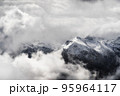 A landscape of the Dolomites Mountain Range covered in the fog under a cloudy sky in Italy 95964117