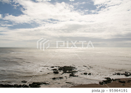 青空と雲と陽射しの下の押し寄せる波とゴロゴロした岩のある海岸 ロンドン郊外のヘイスティングスにて 青空と雲と陽射しの下の押し寄せる波とゴロゴロした岩のある海岸 ロンドン郊外のヘイスティングスにて 95964191