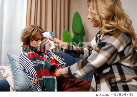 Mature mother measures the temperature with a digital thermometer of her adult daughter who has the flu Mature mother measures the temperature with a digital thermometer of her adult daughter who has the flu 95964749