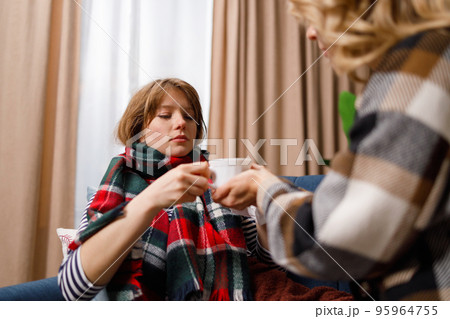 Mother gives a mug of hot tea to her daughter who is sick with the flu 95964755