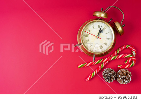 Bronze alarm clock, candy cane and fir cones on red background. Christmas and New Year background Bronze alarm clock, candy cane and fir cones on red background. Christmas and New Year background 95965383