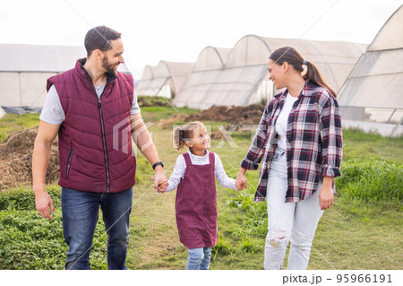 Farming, field and parents holding hands with child walking on farm, bonding and happy together. Agriculture, countryside and family taking walk to check vegetables, crops and growth in greenhouse Farming, field and parents holding hands with child walking on farm, bonding and happy together. Agriculture, countryside and family taking walk to check vegetables, crops and growth in greenhouse 95966191