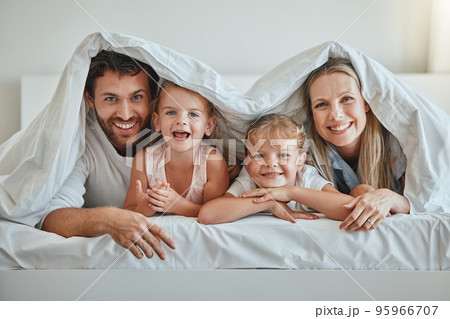 Love, parents and kids under blanket, happy and laugh together for fun, smile and joy. Portrait, family, and have quality time on vacation, holiday and bonding in bedroom for the weekend and cheerful 95966707