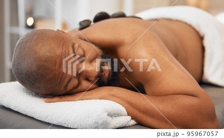 Black man, spa bed hot stone massage and relax body, treatment and luxury physical therapy for health, calm and wellness. Zen man, rest salon and rock for healthcare, recovery or skincare on back Black man, spa bed hot stone massage and relax body, treatment and luxury physical therapy for health, calm and wellness. Zen man, rest salon and rock for healthcare, recovery or skincare on back 95967057