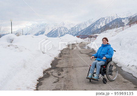 Caucasian woman in a wheelchair travels in the mountains in winter. 95969135