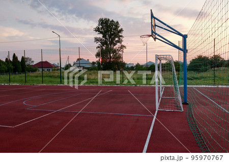 Outdoors mini football and basketball court with ball gate and basket surrounded with high protective fence. Outdoors mini football and basketball court with ball gate and basket surrounded with high protective fence. 95970767