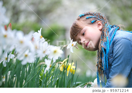 Happy child girl enjoying sweet smell of white narcissus flowers in summer garden Happy child girl enjoying sweet smell of white narcissus flowers in summer garden 95971214