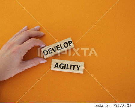 Develop agility symbol. Concept word Develop agility on wooden blocks. Beautiful orange background. Businessman hand. Business and Develop agility concept. Copy space Develop agility symbol. Concept word Develop agility on wooden blocks. Beautiful orange background. Businessman hand. Business and Develop agility concept. Copy space 95972503