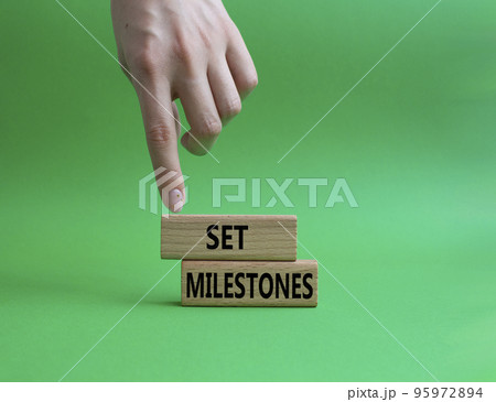 Set milestones symbol. Concept word Set milestones on wooden blocks. Beautiful green background. Businessman hand. Business and Set milestones concept. Copy space 95972894