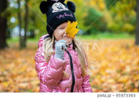 A girl holds a large yellow maple leaf in her hands. 95973363