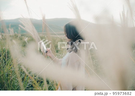 自然の中にスマホを持って佇む女性の写真 95973682