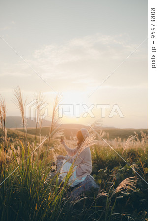 夕暮れの自然の中にスマホで音楽を聴きながら佇む女性の写真 夕暮れの自然の中にスマホで音楽を聴きながら佇む女性の写真 95973808