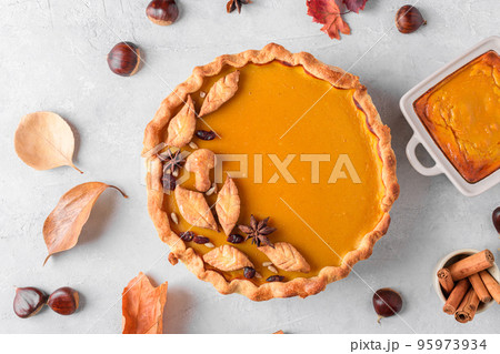 Pumpkin pie with fall leaves on a gray table background with dry autumn leaves and fresh chestnuts, close up Pumpkin pie with fall leaves on a gray table background with dry autumn leaves and fresh chestnuts, close up 95973934